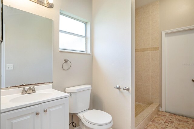 full bathroom featuring a tile shower, vanity, and toilet