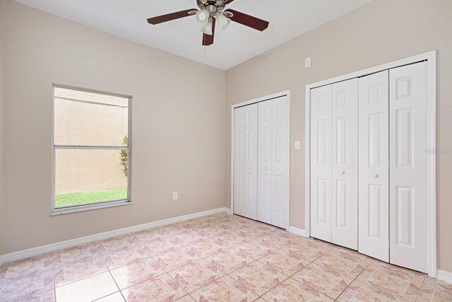 unfurnished bedroom with light tile patterned floors, a textured ceiling, a ceiling fan, baseboards, and multiple closets