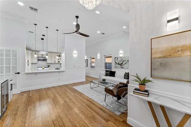 living room with a high ceiling, ceiling fan with notable chandelier, crown molding, and light hardwood / wood-style flooring