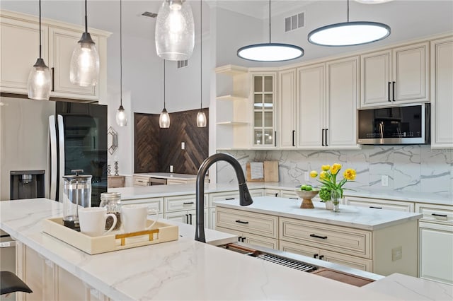 kitchen with appliances with stainless steel finishes, cream cabinets, and hanging light fixtures