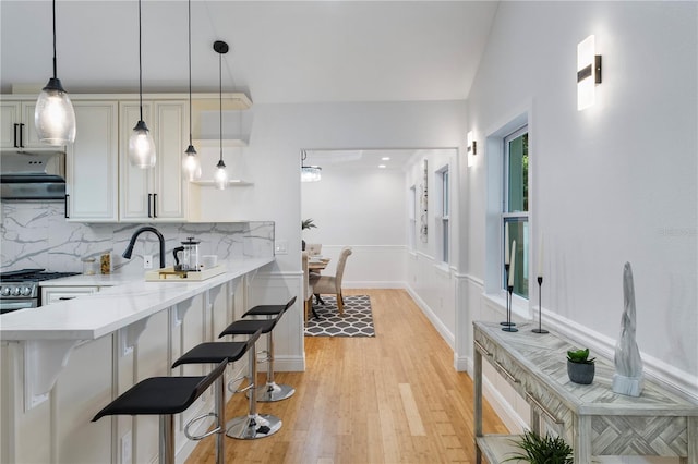 kitchen with a kitchen bar, light stone counters, backsplash, and light hardwood / wood-style floors