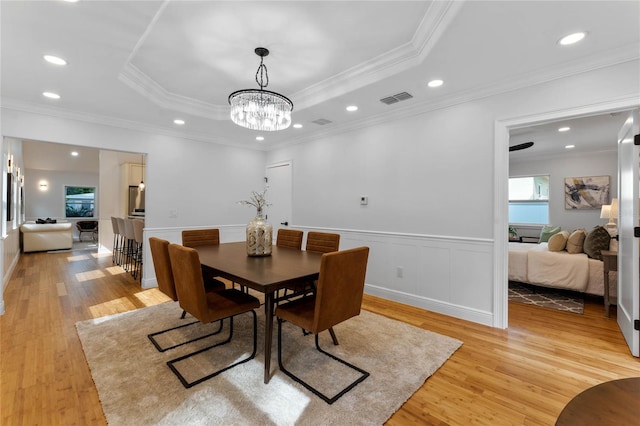 dining room with crown molding, a raised ceiling, and light wood-type flooring