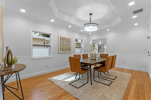 dining area with crown molding, a raised ceiling, an inviting chandelier, and light hardwood / wood-style floors