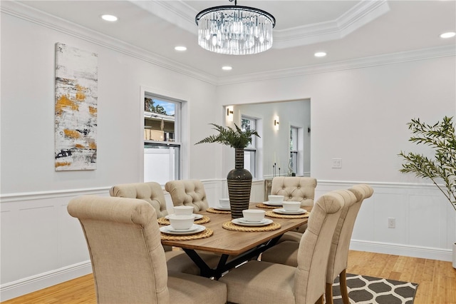 dining space with ornamental molding, a raised ceiling, and light hardwood / wood-style flooring