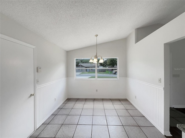 tiled empty room with vaulted ceiling, a textured ceiling, and a chandelier