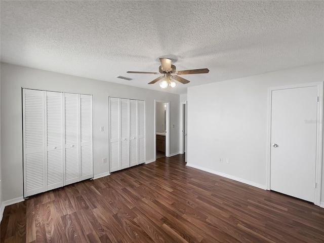 unfurnished bedroom featuring baseboards, visible vents, a ceiling fan, dark wood-style flooring, and two closets