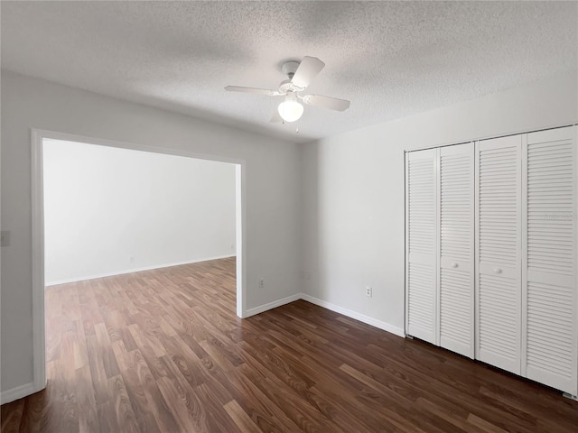 unfurnished bedroom with dark wood-style floors, a closet, ceiling fan, a textured ceiling, and baseboards