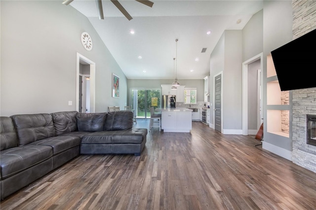 living room with dark wood-type flooring, high vaulted ceiling, ceiling fan, and a stone fireplace