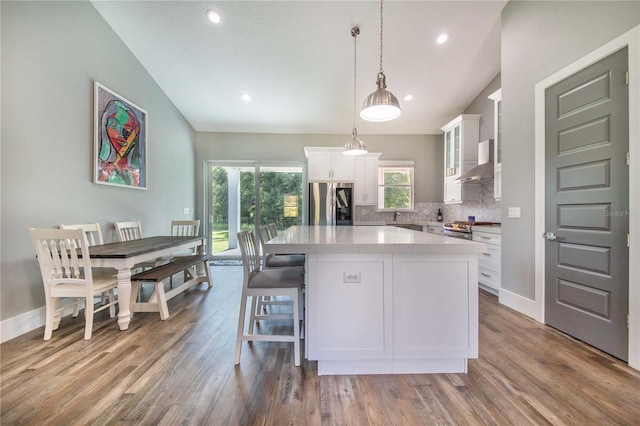 kitchen with stainless steel appliances, a kitchen island, wall chimney exhaust hood, white cabinets, and decorative light fixtures