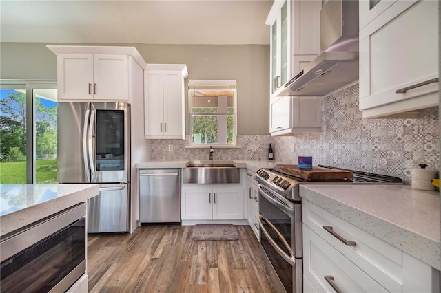 kitchen featuring white cabinets, appliances with stainless steel finishes, wall chimney exhaust hood, and sink