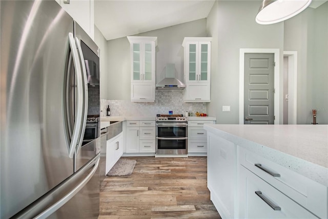 kitchen with vaulted ceiling, stainless steel appliances, wall chimney range hood, decorative backsplash, and white cabinets