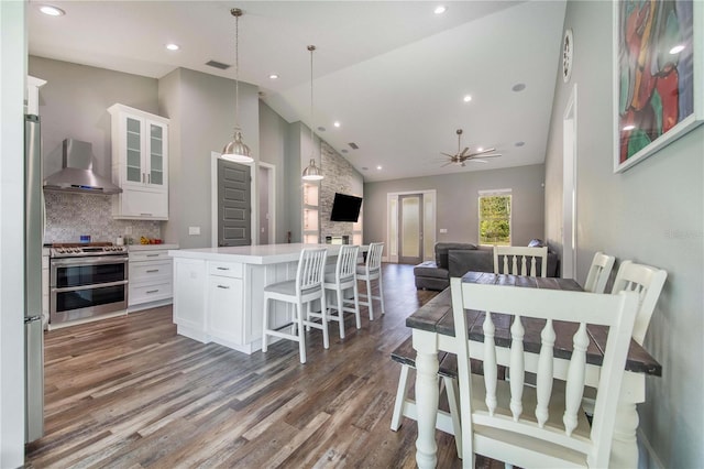 kitchen with white cabinetry, a center island, wall chimney exhaust hood, backsplash, and appliances with stainless steel finishes