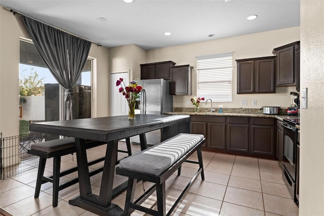 kitchen featuring dark brown cabinets, black electric range, sink, light tile patterned floors, and light stone countertops