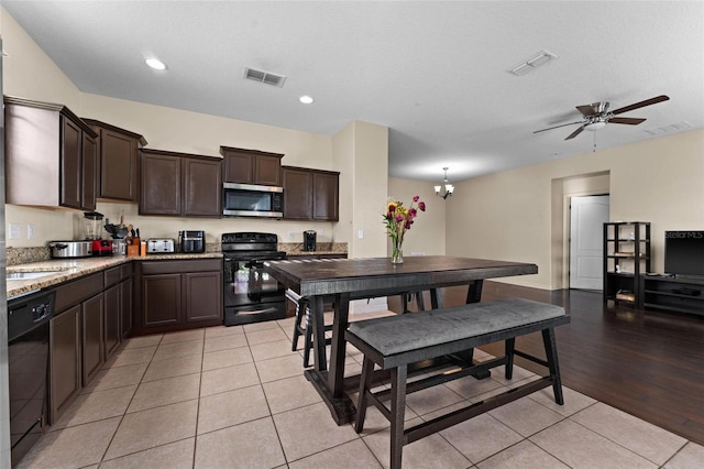 kitchen with light stone counters, ceiling fan with notable chandelier, black appliances, dark brown cabinets, and light hardwood / wood-style flooring