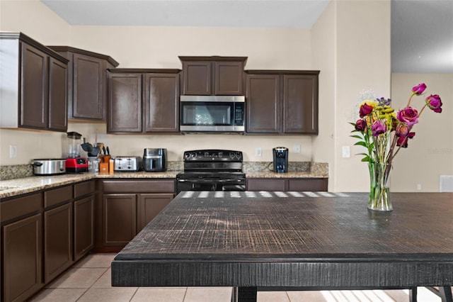 kitchen featuring dark brown cabinetry, light tile patterned flooring, light stone counters, and black range oven