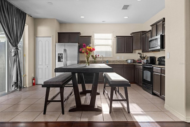 kitchen with appliances with stainless steel finishes, dark brown cabinets, light tile patterned floors, and sink