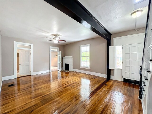 unfurnished living room featuring ceiling fan, beam ceiling, dark hardwood / wood-style flooring, and a fireplace