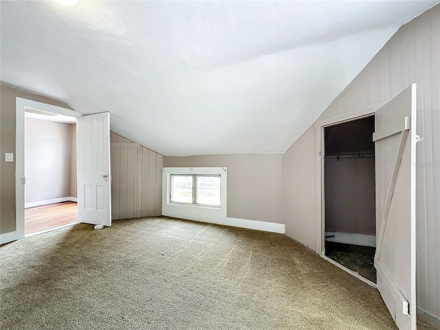 bonus room with vaulted ceiling, wood walls, and carpet floors