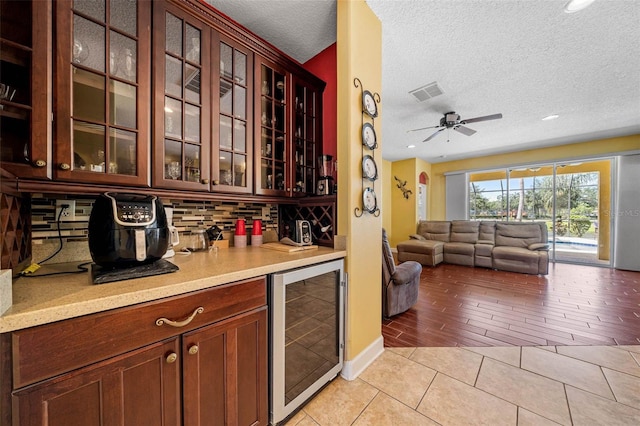 kitchen with a textured ceiling, wine cooler, light hardwood / wood-style flooring, decorative backsplash, and ceiling fan