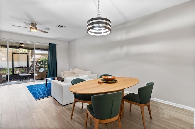 dining space with ceiling fan with notable chandelier and light wood-type flooring