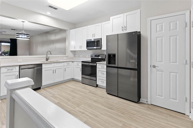 kitchen with light wood-type flooring, stainless steel appliances, white cabinetry, sink, and pendant lighting