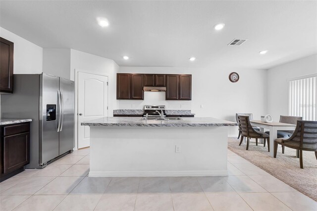 kitchen with light stone countertops, a kitchen island with sink, sink, stainless steel fridge with ice dispenser, and dark brown cabinetry