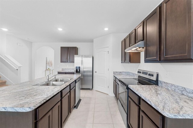 kitchen featuring a center island with sink, light tile patterned floors, stainless steel appliances, sink, and dark brown cabinetry