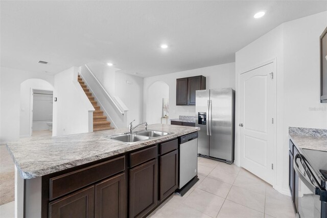 kitchen with dark brown cabinets, light tile patterned floors, appliances with stainless steel finishes, a kitchen island with sink, and sink