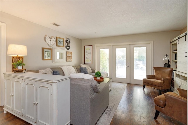 living room featuring french doors, a textured ceiling, dark wood-type flooring, and a barn door