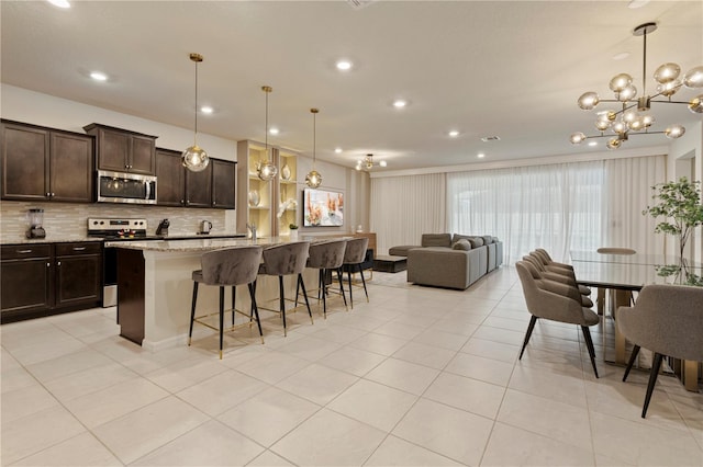 kitchen with pendant lighting, an island with sink, appliances with stainless steel finishes, light stone countertops, and a kitchen bar