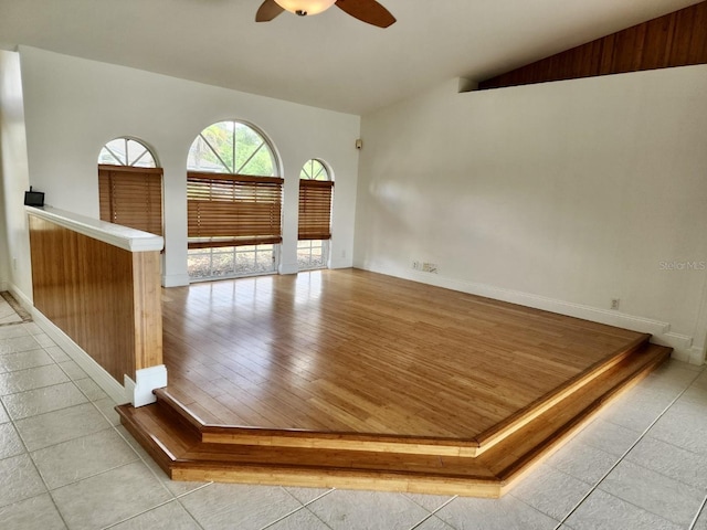 empty room with light tile patterned floors, baseboards, a ceiling fan, and vaulted ceiling