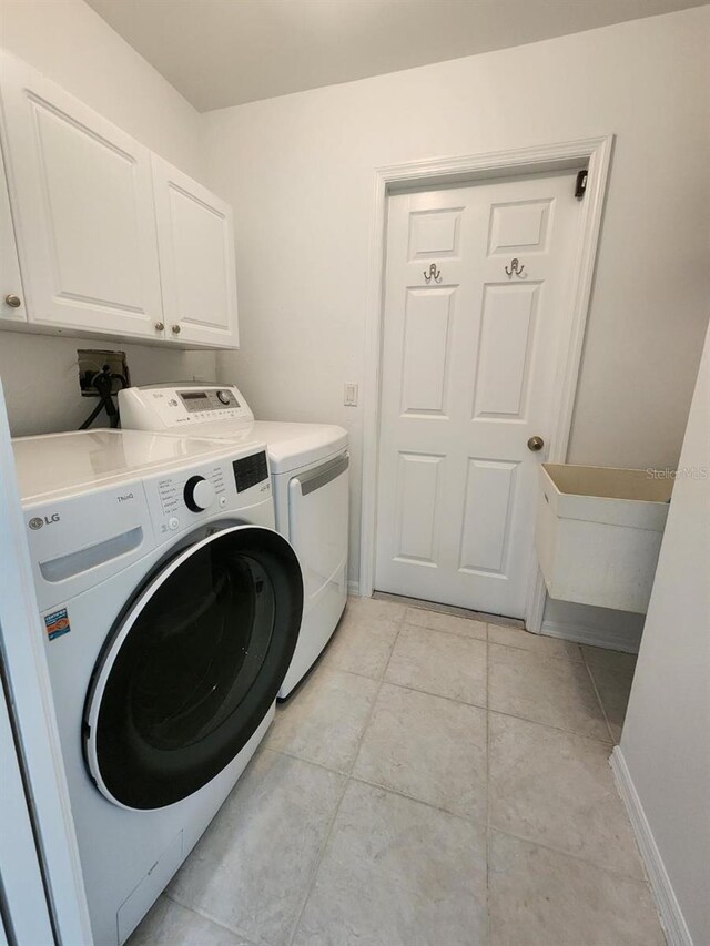 washroom with light tile patterned flooring, cabinets, and washing machine and dryer