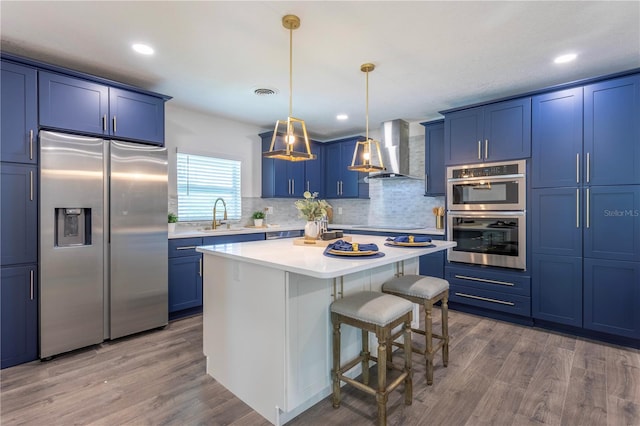 kitchen featuring blue cabinetry, wall chimney range hood, stainless steel appliances, and wood-type flooring