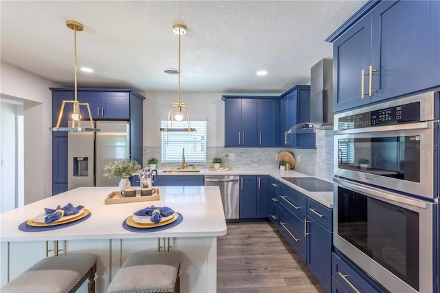 kitchen with wall chimney range hood, a breakfast bar area, appliances with stainless steel finishes, blue cabinetry, and sink