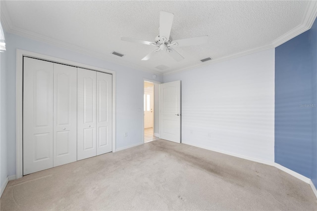 unfurnished bedroom featuring ceiling fan, a textured ceiling, light carpet, a closet, and ornamental molding