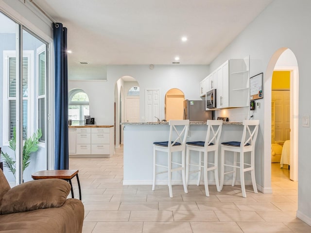 kitchen with kitchen peninsula, light stone countertops, appliances with stainless steel finishes, a breakfast bar area, and white cabinets