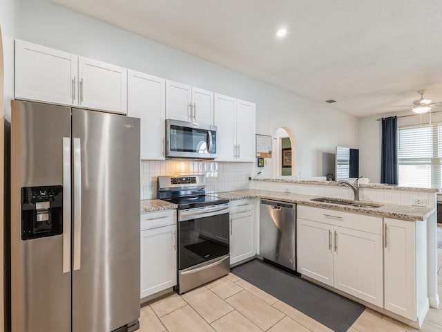 kitchen featuring light stone countertops, appliances with stainless steel finishes, kitchen peninsula, ceiling fan, and white cabinets