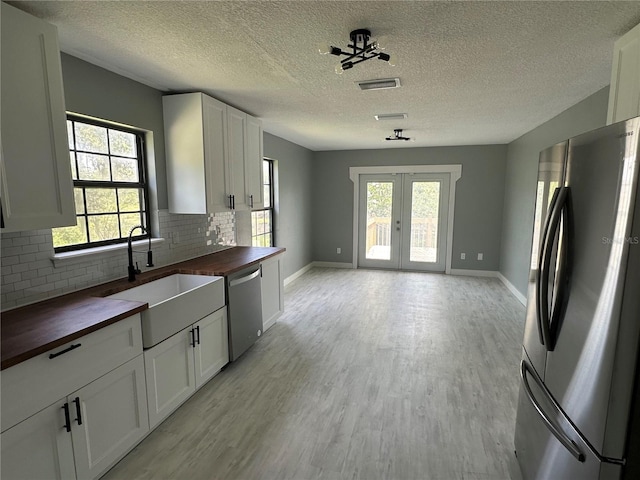 kitchen with a sink, appliances with stainless steel finishes, butcher block counters, light wood finished floors, and a healthy amount of sunlight