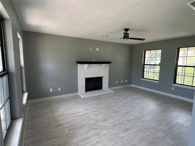 unfurnished living room featuring a brick fireplace, wood finished floors, baseboards, and ceiling fan