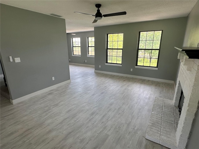 unfurnished living room featuring visible vents, a textured ceiling, wood finished floors, baseboards, and a brick fireplace