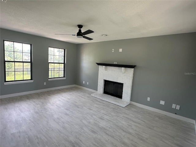 unfurnished living room with a fireplace, a textured ceiling, baseboards, and wood finished floors