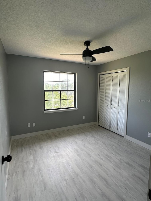 unfurnished bedroom with a ceiling fan, a textured ceiling, wood finished floors, a closet, and baseboards