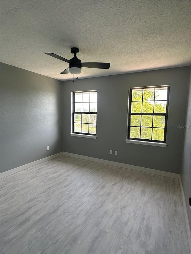 empty room with a textured ceiling, a ceiling fan, baseboards, and wood finished floors