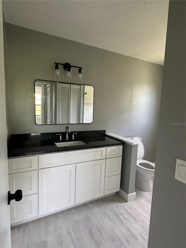 bathroom with a textured ceiling, wood finished floors, vanity, and toilet