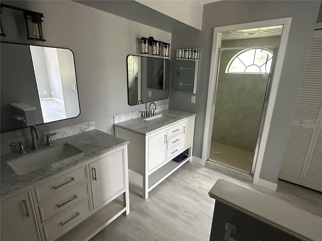 full bath with a shower stall, two vanities, wood finished floors, and a sink