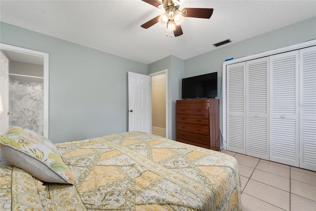 bedroom featuring a textured ceiling, light tile patterned flooring, ceiling fan, and a closet