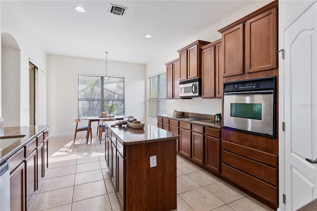 kitchen with appliances with stainless steel finishes, a kitchen island, pendant lighting, and light tile patterned flooring