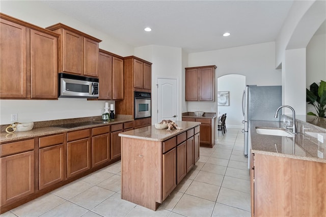 kitchen featuring stone countertops, light tile patterned floors, a kitchen island, sink, and appliances with stainless steel finishes