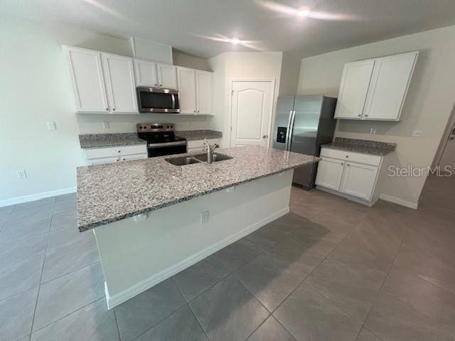 kitchen with light stone countertops, white cabinets, stainless steel appliances, sink, and a center island with sink