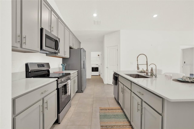 kitchen with appliances with stainless steel finishes, gray cabinetry, sink, washer / dryer, and light tile patterned flooring